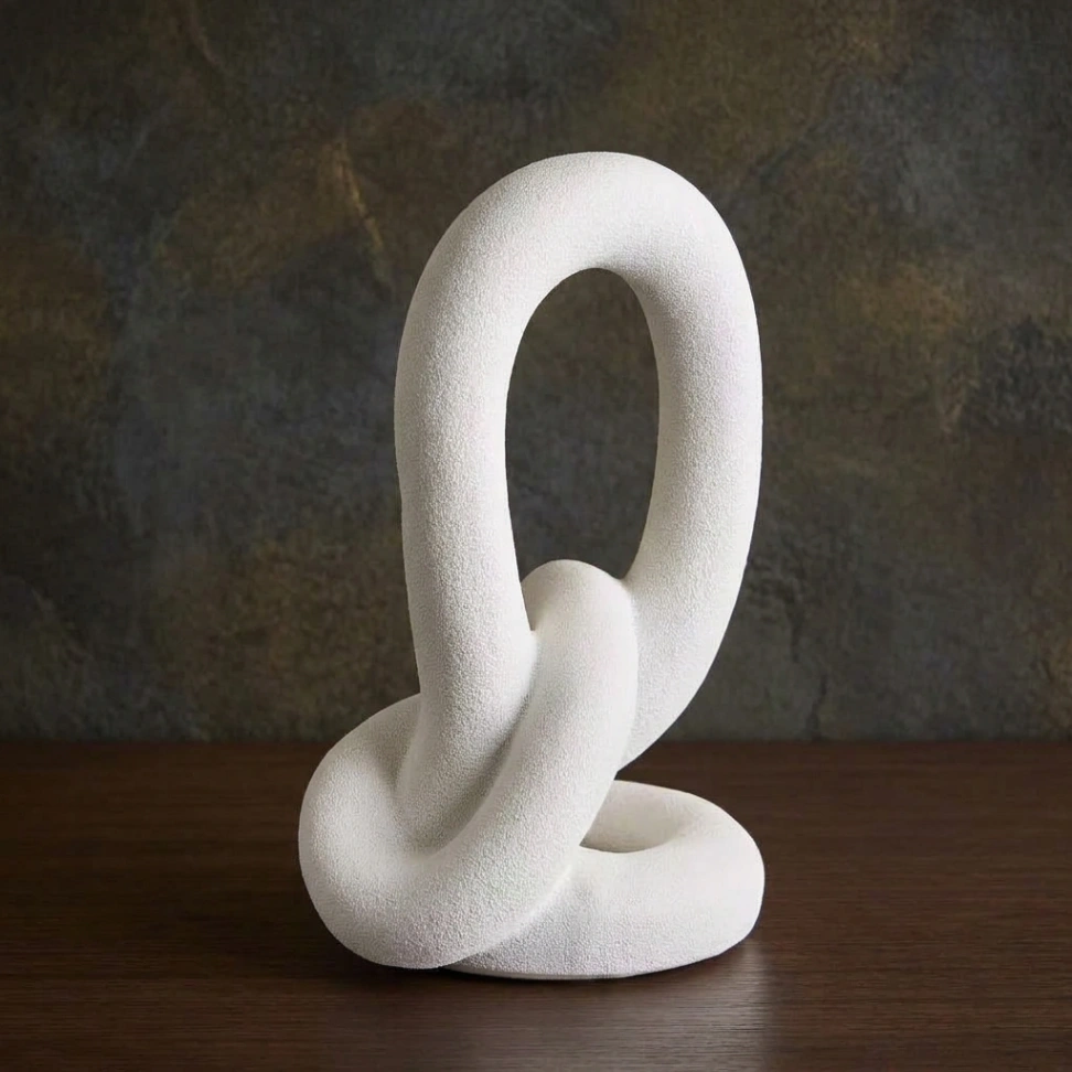 White ceramic abstract decorative sculpture with an interlocking-loop design and matte finish, styled for minimalist décor in a studio-apartment living room.